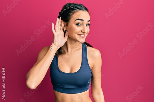 Young brunette girl wearing sportswear and braids smiling with hand over ear listening an hearing to rumor or gossip. deafness concept. © Krakenimages.com