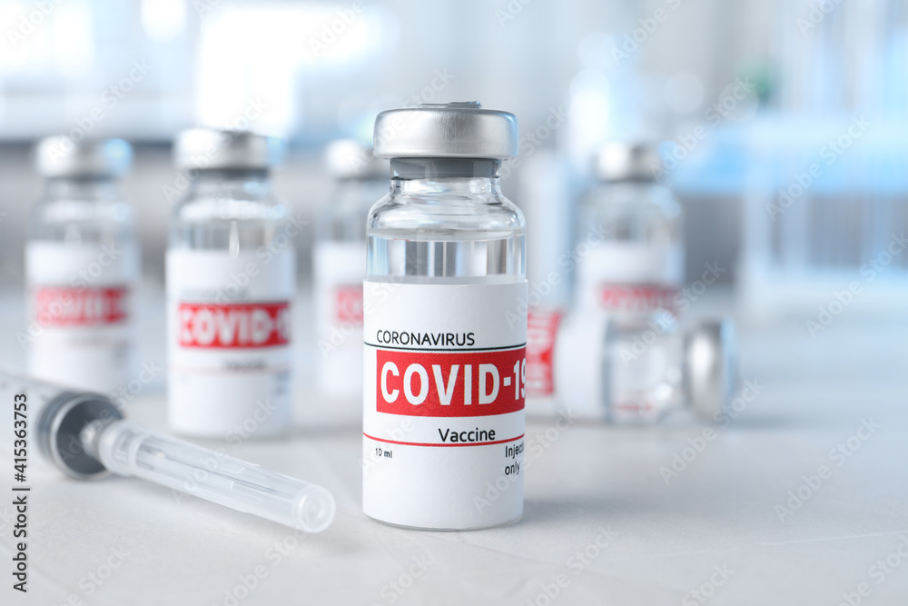 Glass vials with COVID-19 vaccine and syringe on light table Glass vials with COVID-19 vaccine and syringe on light table