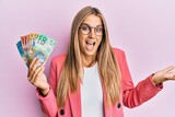 Young blonde woman wearing business style holding australian dollars celebrating achievement with happy smile and winner expression with raised hand