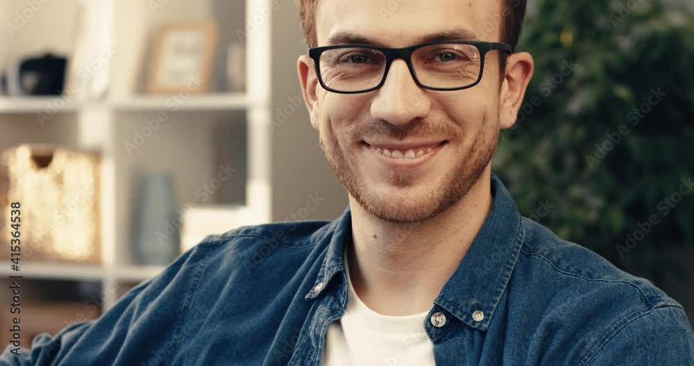 Close-up portrait of handsome bearded man with glasses sitting at home on sofa and looking at camera smiling. Close-up portrait of handsome bearded man with glasses sitting at home on sofa and looking at camera smiling.