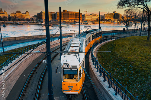 A yellow tram travels along the banks of the Danube. Sunset view. 