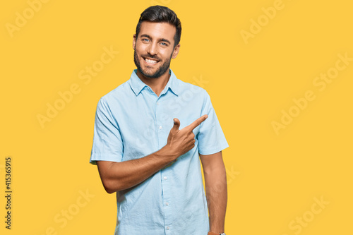 Handsome hispanic man wearing casual clothes cheerful with a smile of face pointing with hand and finger up to the side with happy and natural expression on face
