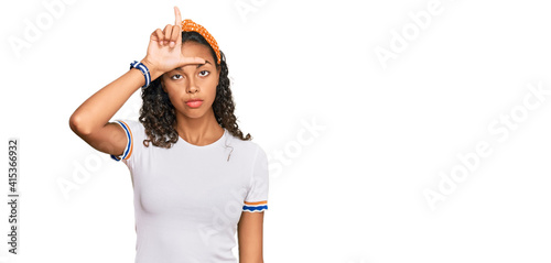 Young african american girl wearing casual clothes making fun of people with fingers on forehead doing loser gesture mocking and insulting.