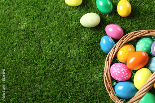 Wicker basket with Easter eggs on green grass, flat lay. Space for text