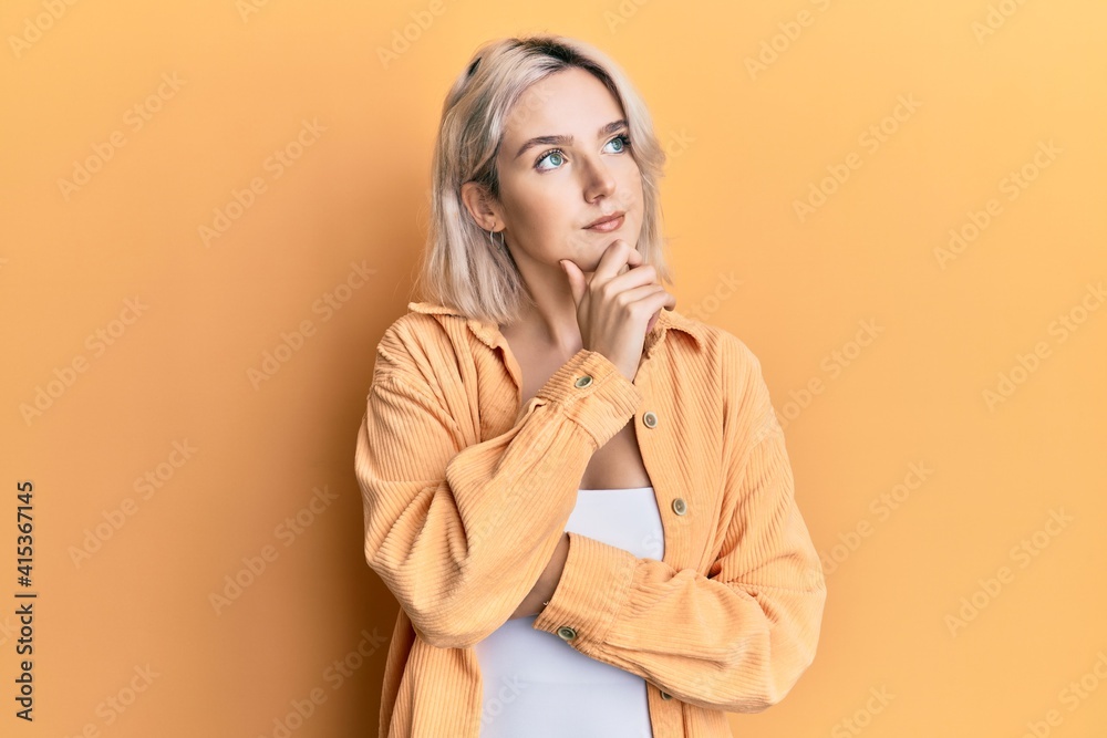 Young blonde girl wearing casual clothes with hand on chin thinking about question, pensive expression. smiling with thoughtful face. doubt concept. Young blonde girl wearing casual clothes with hand on chin thinking about question, pensive expression. smiling with thoughtful face. doubt concept.