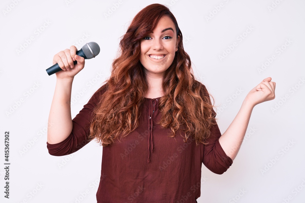 Young beautiful woman singing song using microphone screaming proud, celebrating victory and success very excited with raised arm