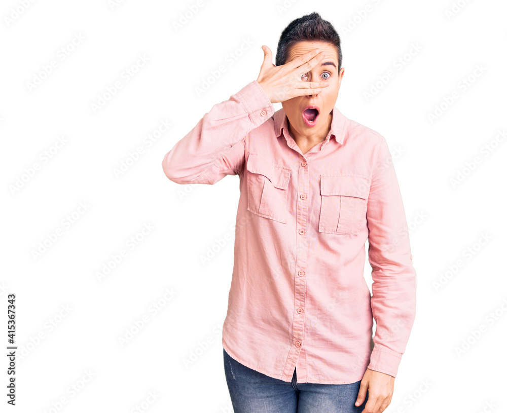 Young woman with short hair wearing casual clothes peeking in shock covering face and eyes with hand, looking through fingers with embarrassed expression. Young woman with short hair wearing casual clothes peeking in shock covering face and eyes with hand, looking through fingers with embarrassed expression.