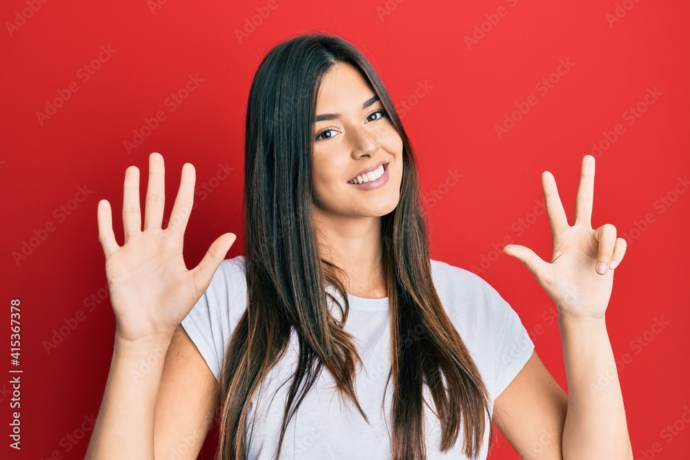 Young brunette woman wearing casual white tshirt over red background showing and pointing up with fingers number eight while smiling confident and happy.