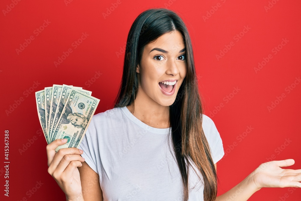 Young brunette woman holding 20 dollars banknote celebrating achievement with happy smile and winner expression with raised hand Young brunette woman holding 20 dollars banknote celebrating achievement with happy smile and winner expression with raised hand