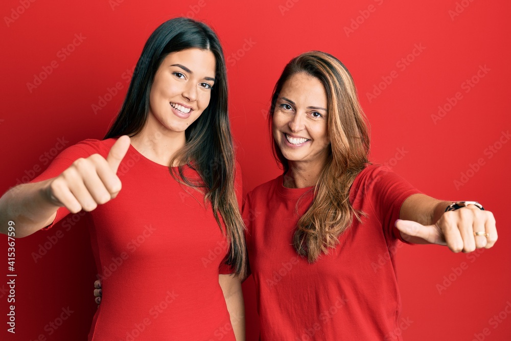 Hispanic family of mother and daughter wearing casual clothes over red background approving doing positive gesture with hand, thumbs up smiling and happy for success. winner gesture. Hispanic family of mother and daughter wearing casual clothes over red background approving doing positive gesture with hand, thumbs up smiling and happy for success. winner gesture.