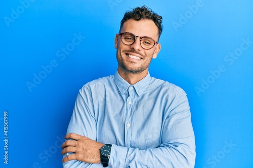 Young hispanic man wearing casual clothes and glasses happy face smiling with crossed arms looking at the camera. positive person.