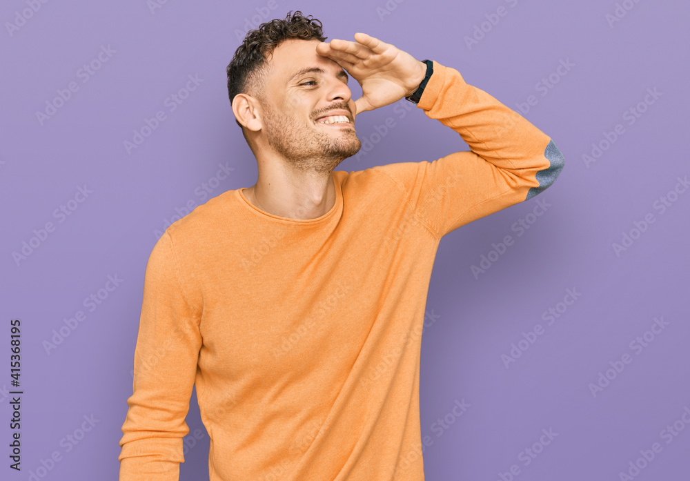 Young hispanic man wearing casual clothes very happy and smiling looking far away with hand over head. searching concept. Young hispanic man wearing casual clothes very happy and smiling looking far away with hand over head. searching concept.