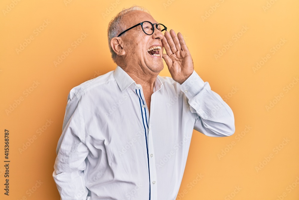 Senior caucasian man wearing casual clothes and glasses shouting and screaming loud to side with hand on mouth. communication concept. Senior caucasian man wearing casual clothes and glasses shouting and screaming loud to side with hand on mouth. communication concept.
