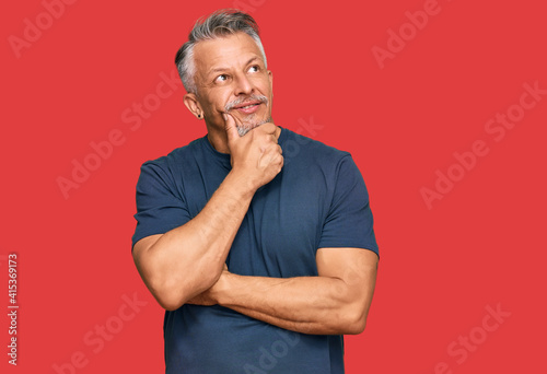 Middle age grey-haired man wearing casual clothes with hand on chin thinking about question, pensive expression. smiling with thoughtful face. doubt concept.