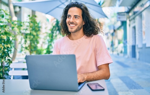 Young hispanic man smiling happy working using laptop at terrace of coffee shop.