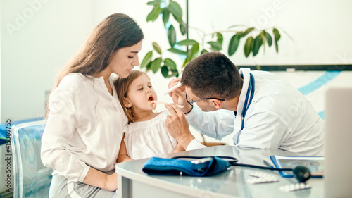 Male Doctor Pediatrician Examining an Ill Sad Kid Girl at Medical Visit With Mother in the Hospital. Male Family Doctor Examining and Consulting to Mother and Her Ill Child.