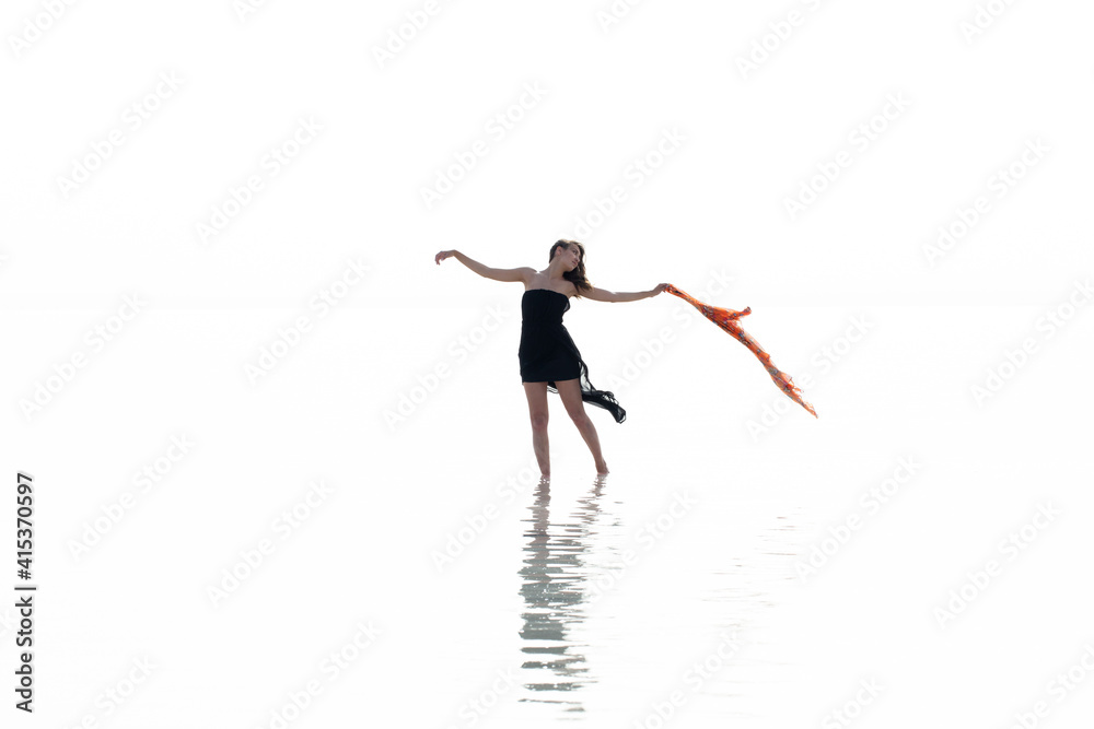 Beautiful woman on the beach, attractive slim model wearing black dress and dancing with a scarf, enjoying summer holidays. Sea, coast, woman and water reflection Beautiful woman on the beach, attractive slim model wearing black dress and dancing with a scarf, enjoying summer holidays. Sea, coast, woman and water reflection
