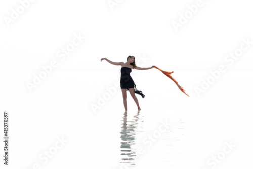 Beautiful woman on the beach, attractive slim model wearing black dress and dancing with a scarf, enjoying summer holidays. Sea, coast, woman and water reflection 