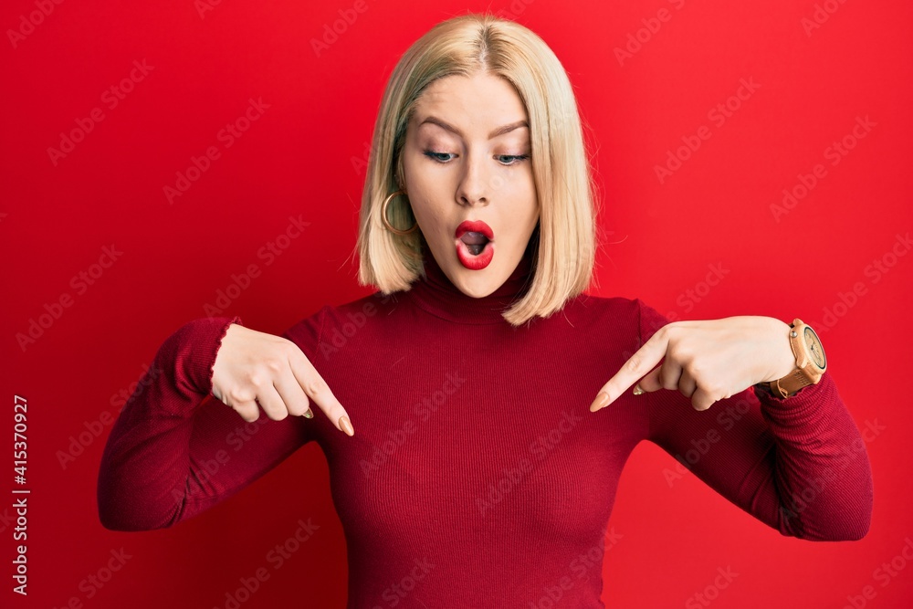 Young blonde woman wearing casual clothes pointing down with fingers showing advertisement, surprised face and open mouth Young blonde woman wearing casual clothes pointing down with fingers showing advertisement, surprised face and open mouth
