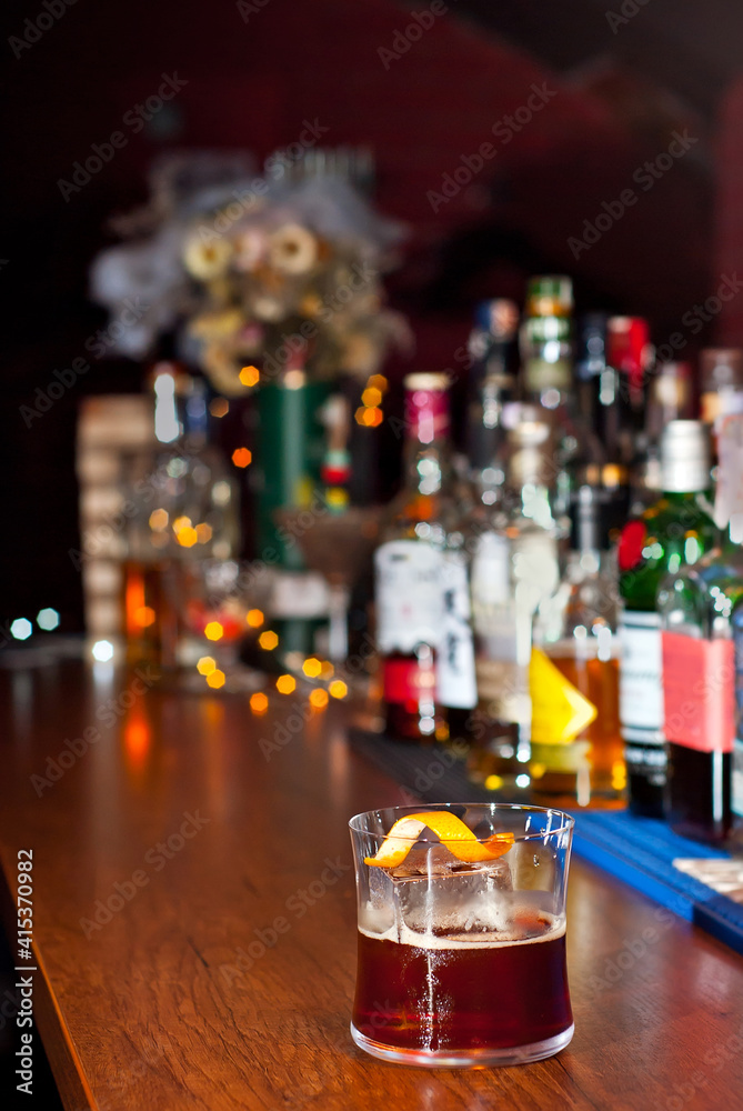 Yellow cocktail on bar counter. Whiskey, rum or brandy on the background of bottles with alcohol. Glass with booze on a wooden board.