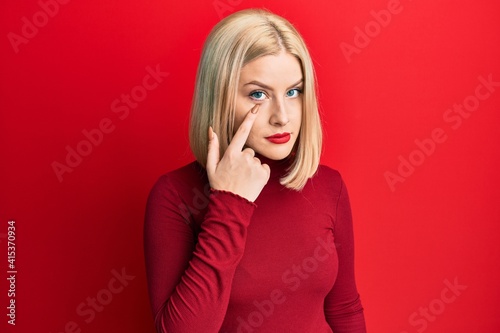 Young blonde woman wearing casual clothes pointing to the eye watching you gesture, suspicious expression