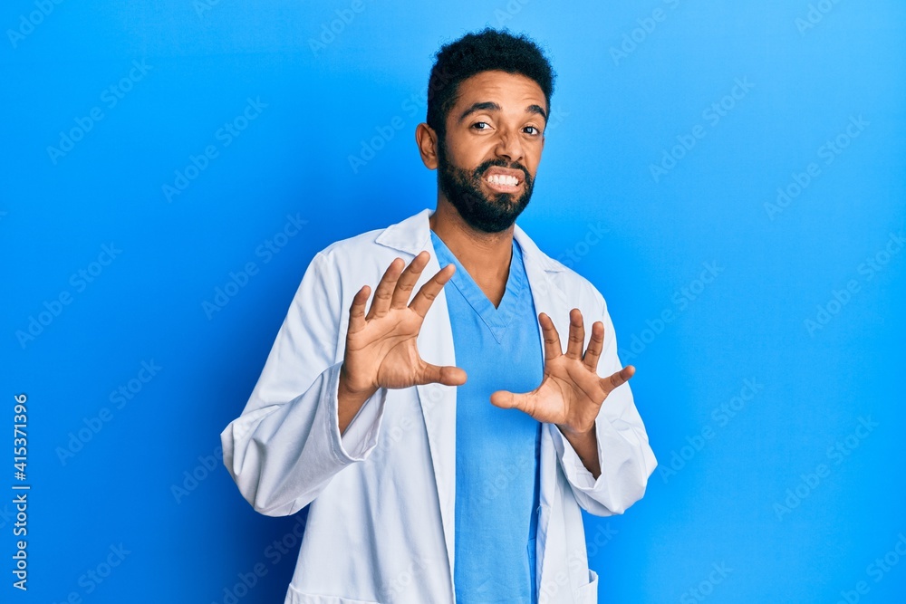 Handsome hispanic man with beard wearing doctor uniform disgusted expression, displeased and fearful doing disgust face because aversion reaction. with hands raised