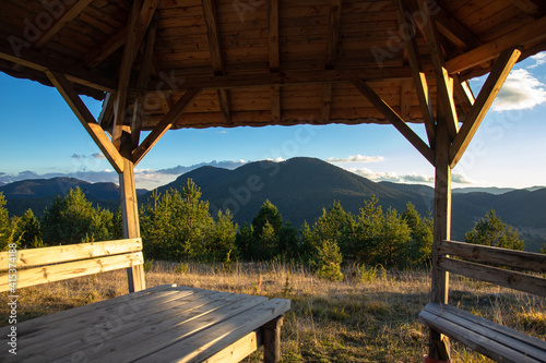wooden gazebo in the mountains at sunset with forest and mountain views. Wooden table and benches