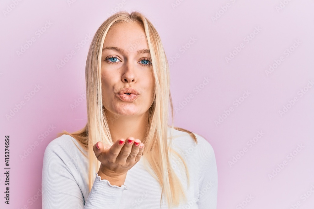 Young blonde girl wearing casual clothes looking at the camera blowing a kiss with hand on air being lovely and sexy. love expression. Young blonde girl wearing casual clothes looking at the camera blowing a kiss with hand on air being lovely and sexy. love expression.