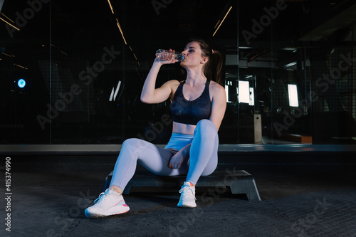 Sportswoman sitting on step platform looking at camera. There is a water bottle in her hand.