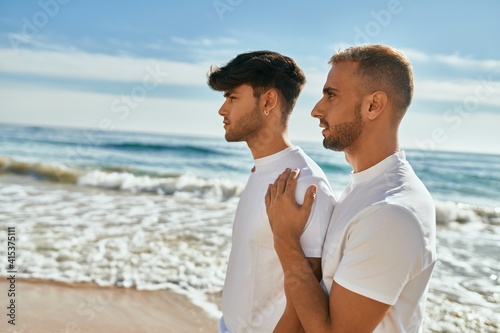 Young gay couple with serious expression looking to the horizon at the beach.