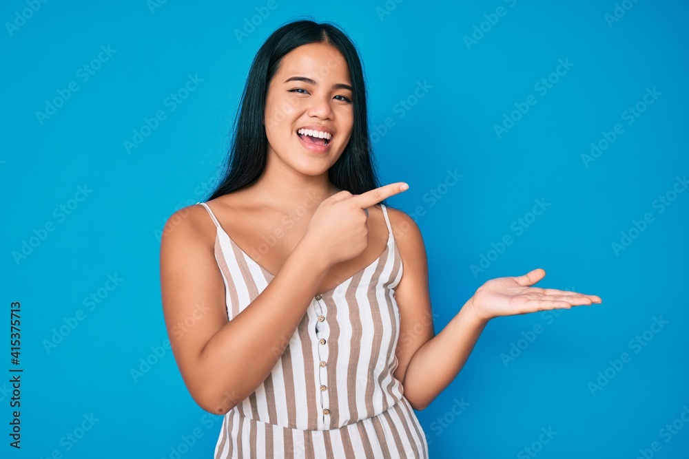 Young beautiful asian girl wearing casual clothes amazed and smiling to the camera while presenting with hand and pointing with finger. Young beautiful asian girl wearing casual clothes amazed and smiling to the camera while presenting with hand and pointing with finger.