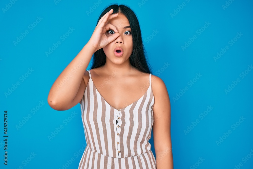 Young beautiful asian girl wearing casual clothes doing ok gesture shocked with surprised face, eye looking through fingers. unbelieving expression.