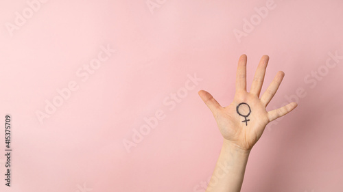 Female hand with female symbol of Venus on pink background for international womens day