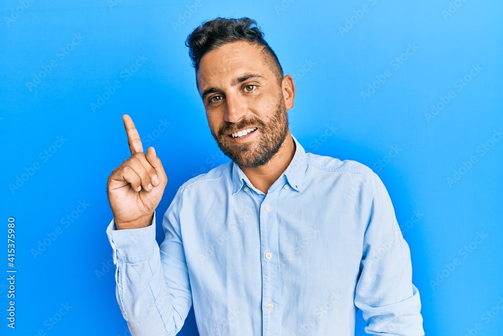 Handsome man with beard wearing casual clothes showing and pointing up with finger number one while smiling confident and happy. Handsome man with beard wearing casual clothes showing and pointing up with finger number one while smiling confident and happy.