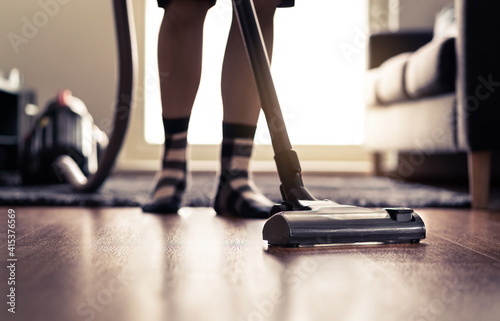 Vacuum cleaner. Man cleaning floor at home and doing household chores in modern apartment. Sun light from window. Happy person vacuuming living room. Tidy house. Cleanliness and housework concept.