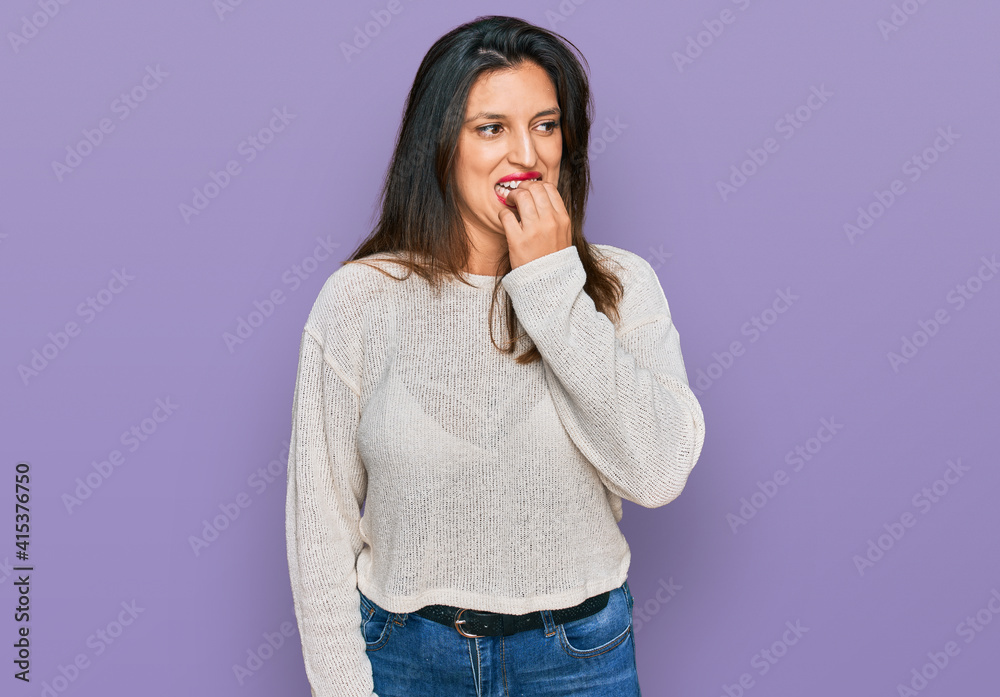 Beautiful hispanic woman wearing casual sweater looking stressed and nervous with hands on mouth biting nails. anxiety problem. Beautiful hispanic woman wearing casual sweater looking stressed and nervous with hands on mouth biting nails. anxiety problem.