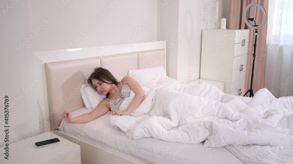 Female Blogger Recording Vlog Video on smartphone waking up in bed. Online Influencer scrolling. Selfie, waving hello in the morning Female Blogger Recording Vlog Video on smartphone waking up in bed. Online Influencer scrolling. Selfie, waving hello in the morning
