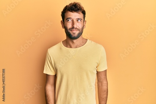 Handsome man with beard wearing casual yellow tshirt over yellow background smiling looking to the side and staring away thinking.