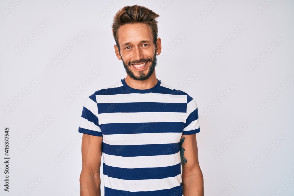 Handsome caucasian man with beard wearing casual striped t-shirt looking positive and happy standing and smiling with a confident smile showing teeth Handsome caucasian man with beard wearing casual striped t-shirt looking positive and happy standing and smiling with a confident smile showing teeth