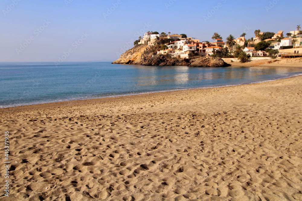 Obraz premium Playa de Bolnuevo, en Mazarrón (Murcia-España). Arena de la playa y superficie del mar en calma, con algunas casas junto al Mediterráneo.