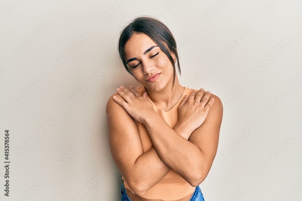 Fototapeta premium Young brunette woman wearing casual clothes hugging oneself happy and positive, smiling confident. self love and self care