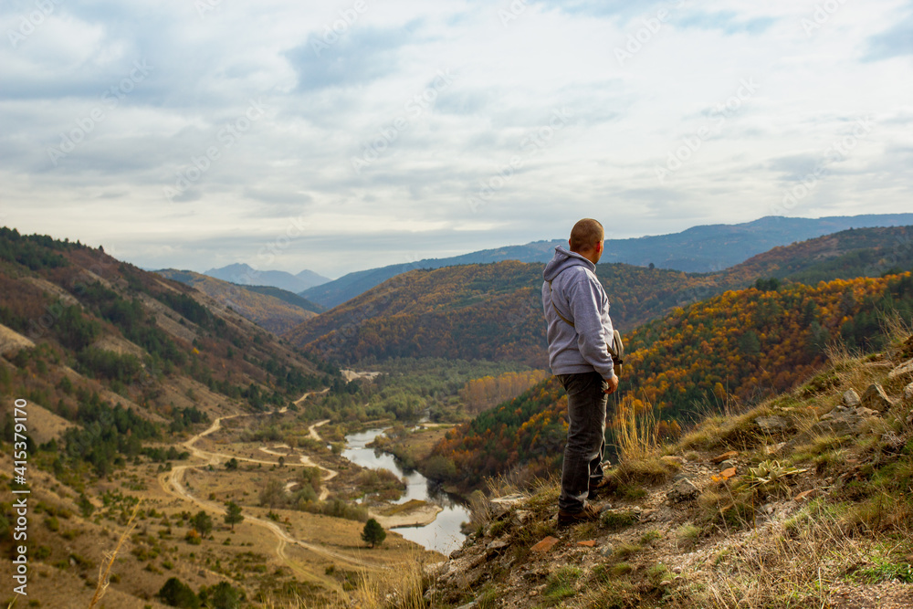 A man at the top of the mountain looks into the distance, against the background of mountains, sky and river. Clear sunny weather in the mountains