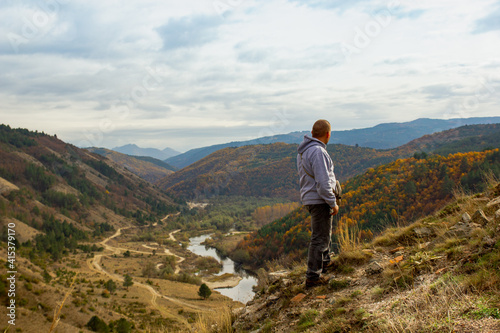 A man at the top of the mountain looks into the distance, against the background of mountains, sky and river. Clear sunny weather in the mountains