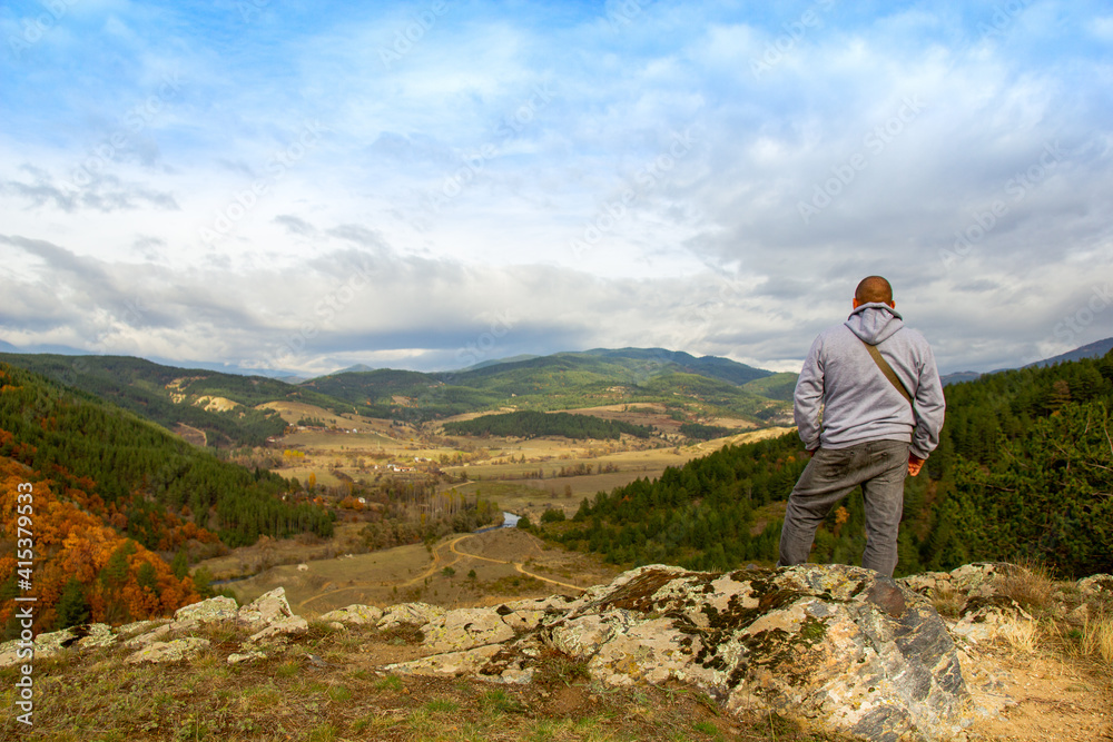 A man at the top of the mountain looks into the distance, against the background of mountains, sky and river. Clear sunny weather in the mountains