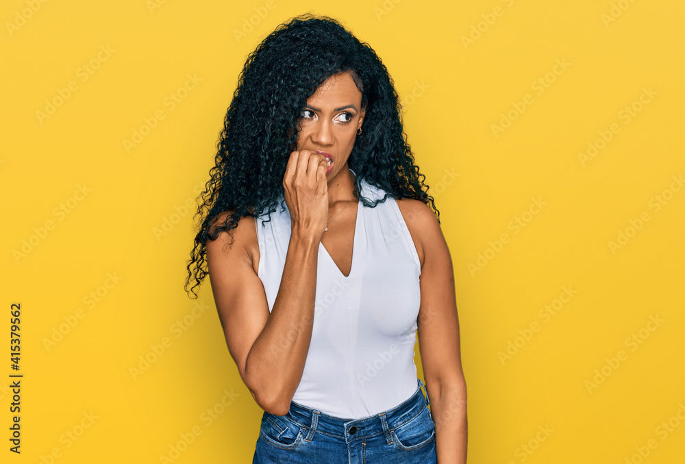 Middle age african american woman wearing casual style with sleeveless shirt looking stressed and nervous with hands on mouth biting nails. anxiety problem. Middle age african american woman wearing casual style with sleeveless shirt looking stressed and nervous with hands on mouth biting nails. anxiety problem.