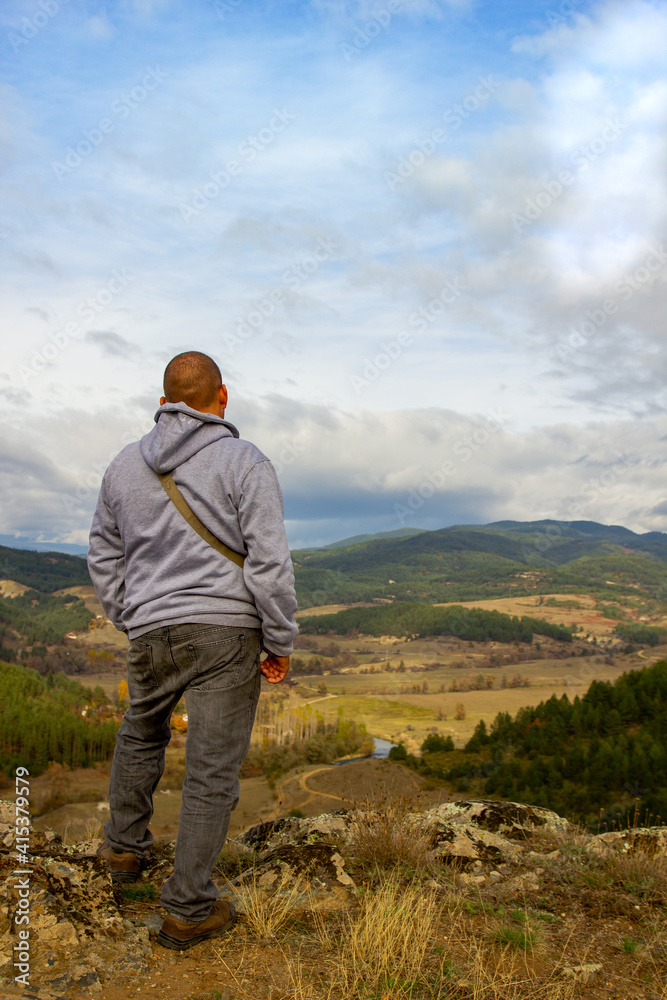 A man at the top of the mountain looks into the distance, against the background of mountains, sky and river. Clear sunny weather in the mountains