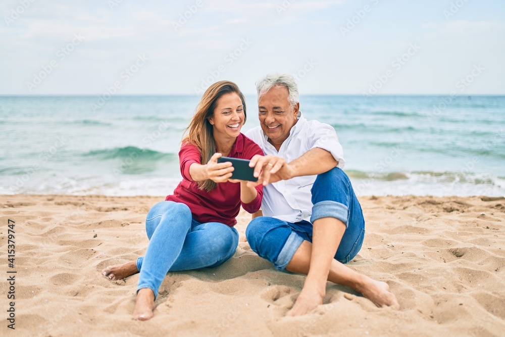 Middle age hispanic couple making selfie by the smartphone at the beach. Middle age hispanic couple making selfie by the smartphone at the beach.
