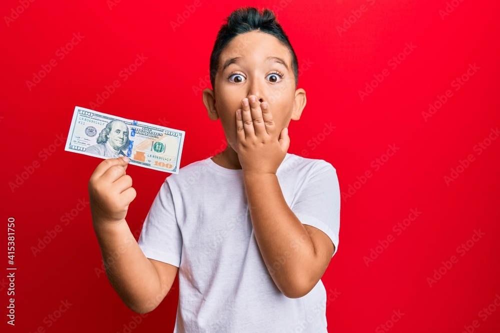 Little boy hispanic kid holding 100 dollars banknote covering mouth with hand, shocked and afraid for mistake. surprised expression Little boy hispanic kid holding 100 dollars banknote covering mouth with hand, shocked and afraid for mistake. surprised expression