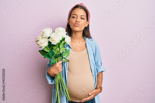 Beautiful hispanic woman expecting a baby holding flowers looking at the camera blowing a kiss being lovely and sexy. love expression. photo