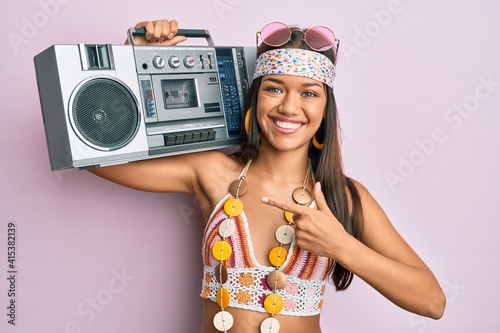 Beautiful hispanic woman wearing hippie style holding boom box smiling happy pointing with hand and finger